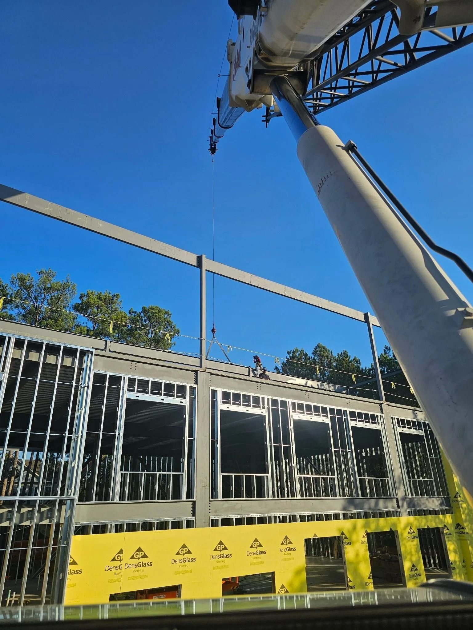 Construction site: crane lifting a steel beam onto a partially built building frame against a blue sky.