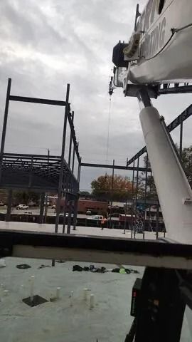 Construction site; crane lifting steel beams; overcast sky.