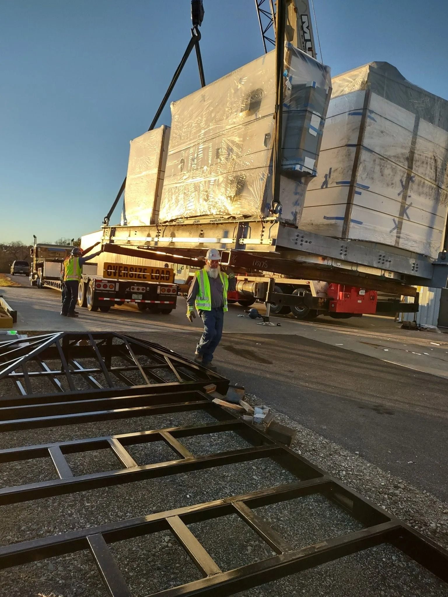 A large, metallic structure being lifted by a crane, with workers observing nearby.