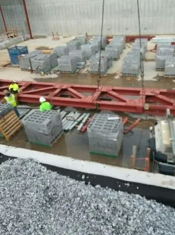 Construction site: Crane lifting pallets of gray blocks near workers wearing hard hats and safety vests.
