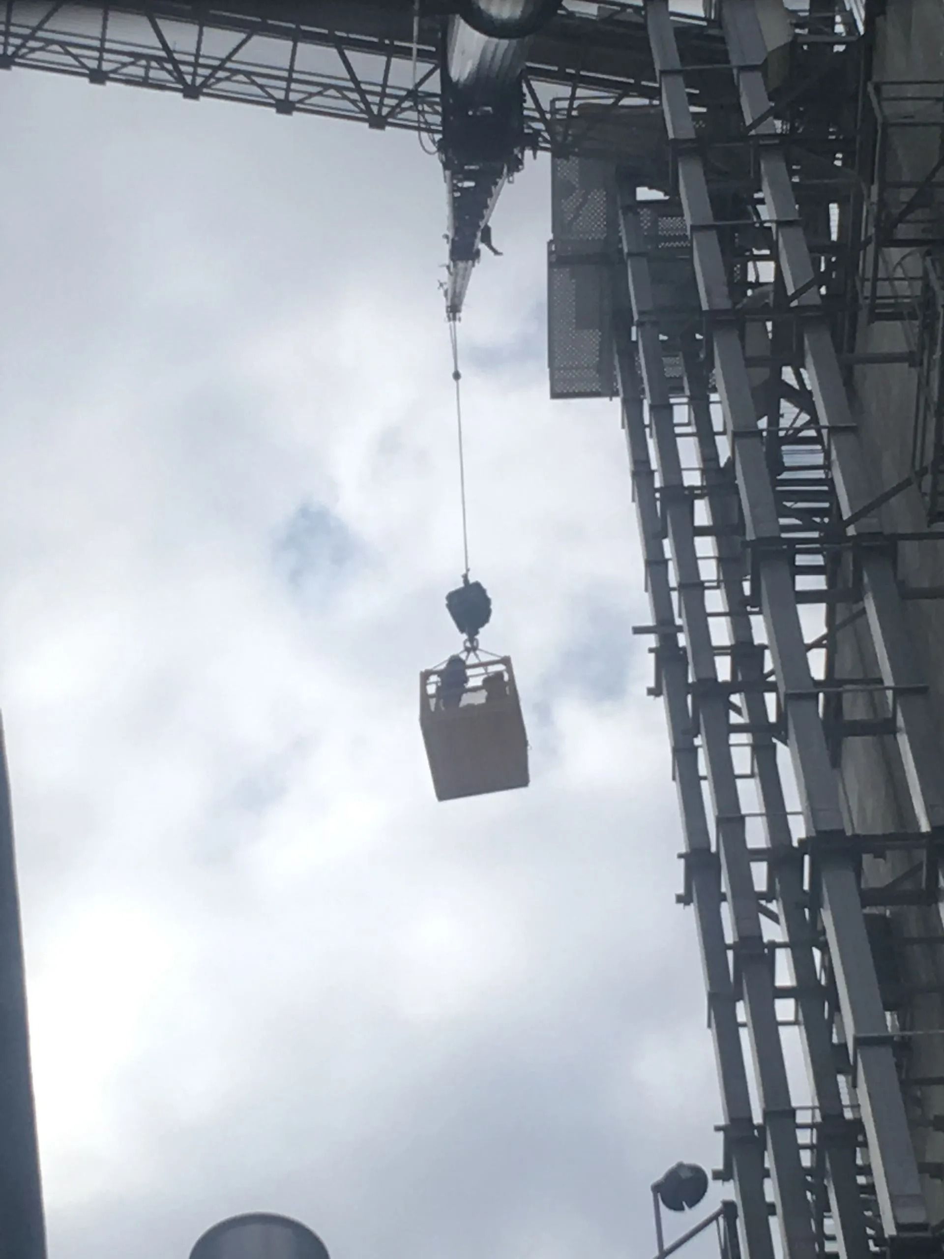 Crane lifting a yellow container high in the air, against a cloudy sky.