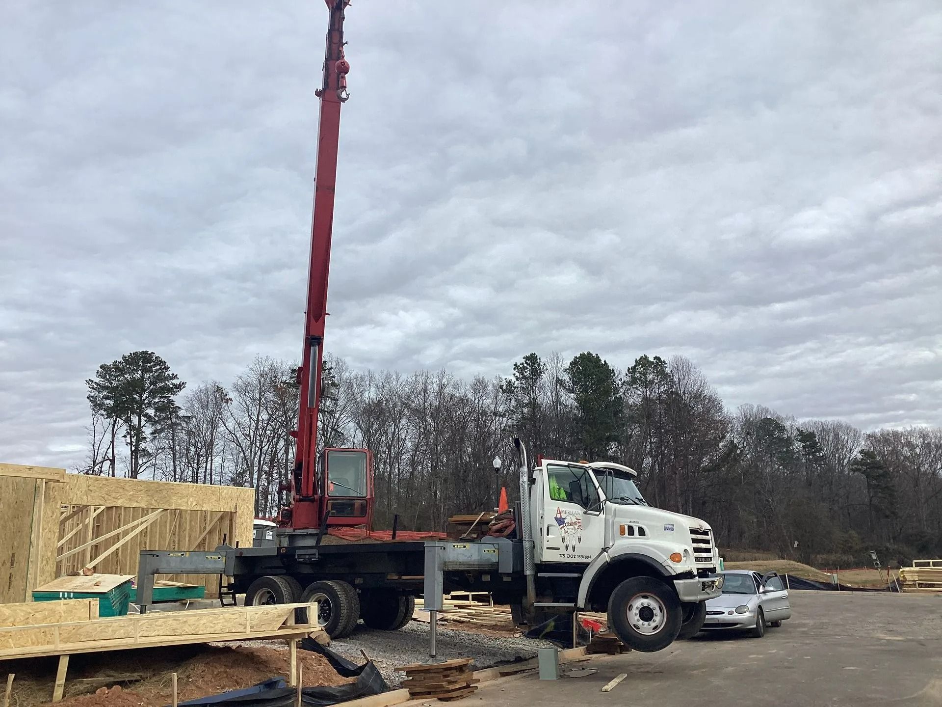 A construction crane on a truck lifting materials at a construction site on a cloudy day.