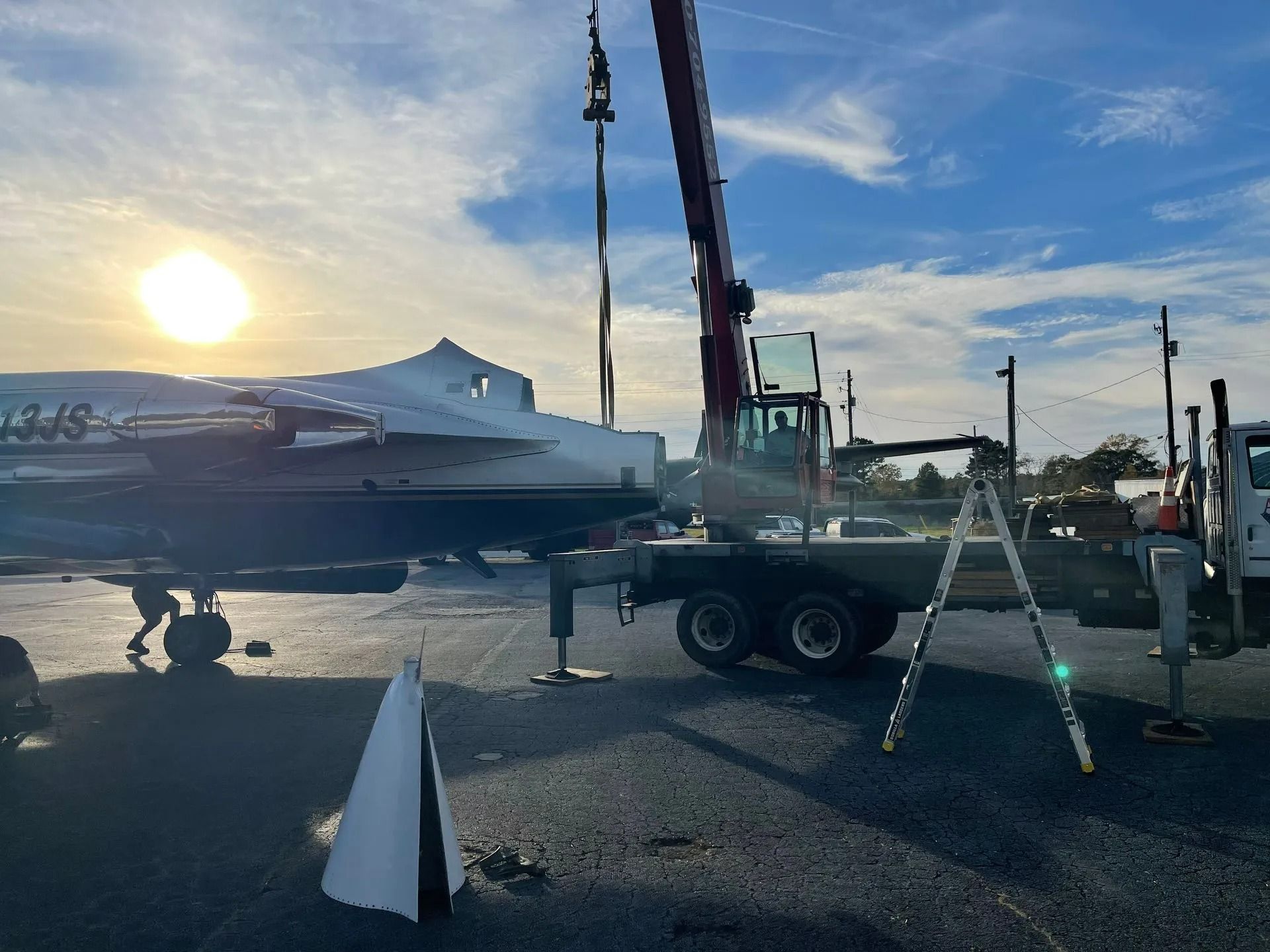 Crane lifting an airplane onto a flatbed truck on a tarmac under a sunny sky.