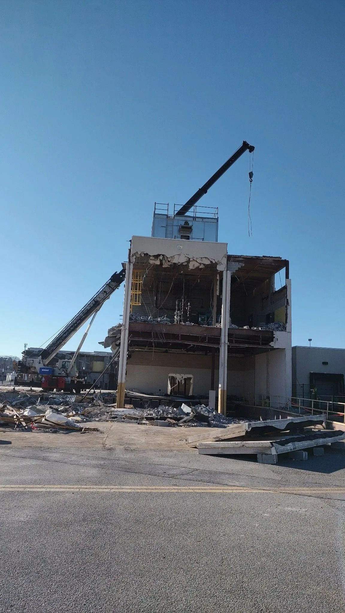 Demolition of a multi-story building, with cranes and debris under a clear blue sky.