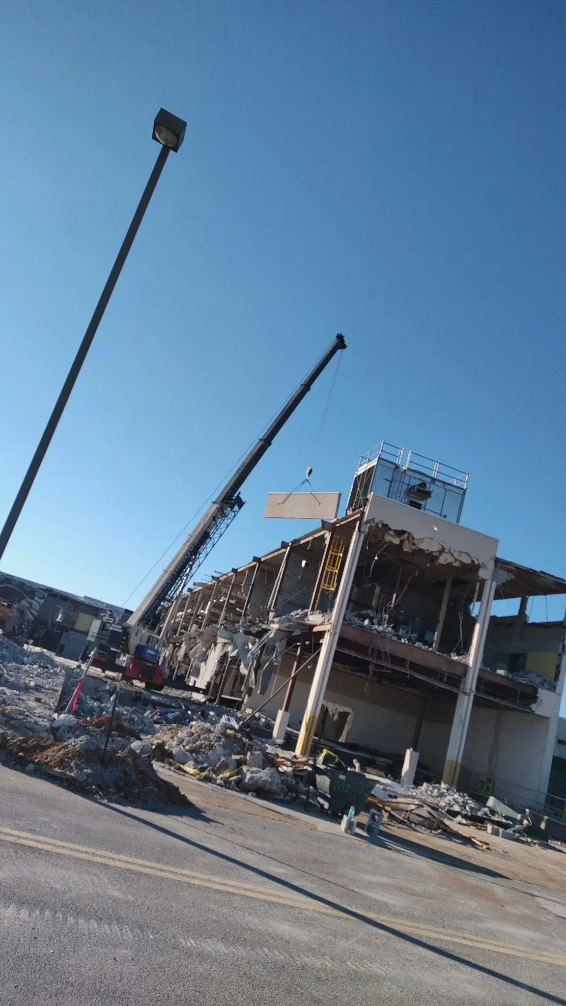 Building demolition with cranes under a clear, blue sky. Debris covers the road.