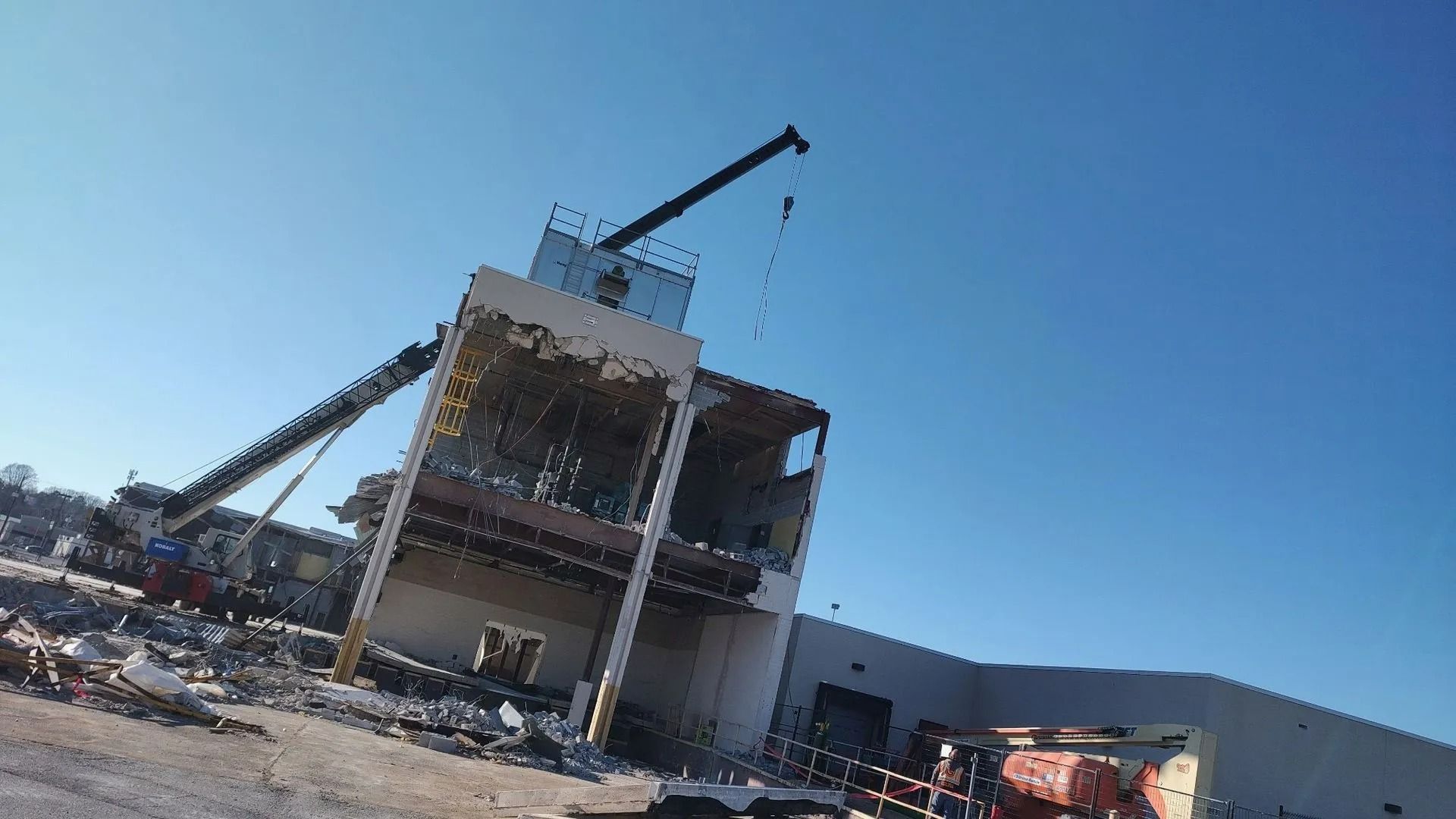 Building demolition with crane against a clear blue sky. Debris scattered below.