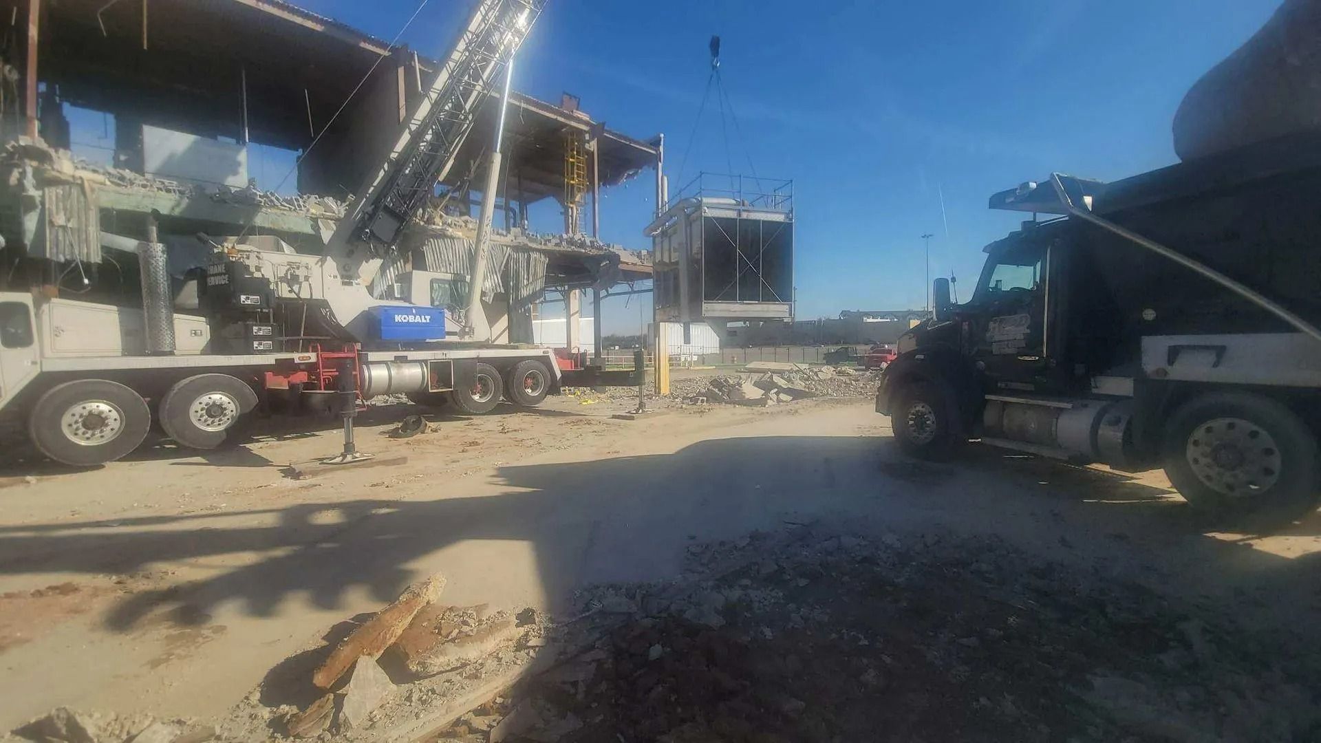 Construction site with a crane lifting debris from a building being demolished, and a dump truck.