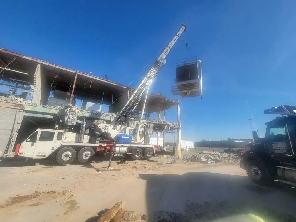 Crane lifting a large sign from a partially demolished building under a clear blue sky.