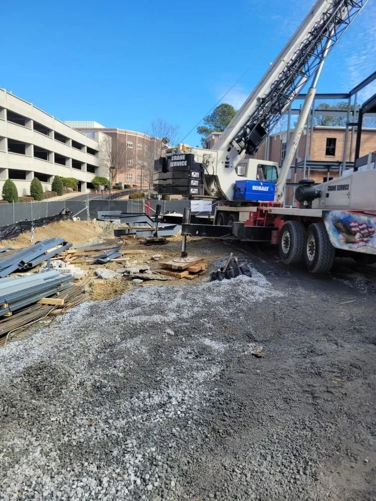 Construction site with crane, gravel, and building in background under blue sky.