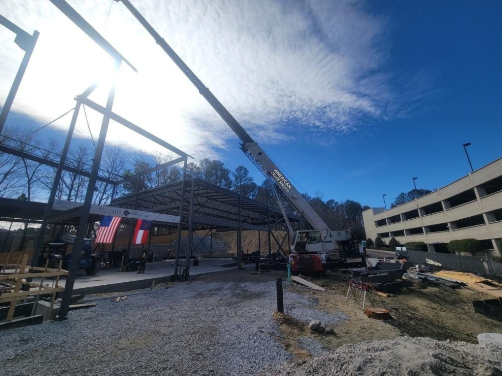 Construction site with a crane lifting steel beams under a bright sun and blue sky.