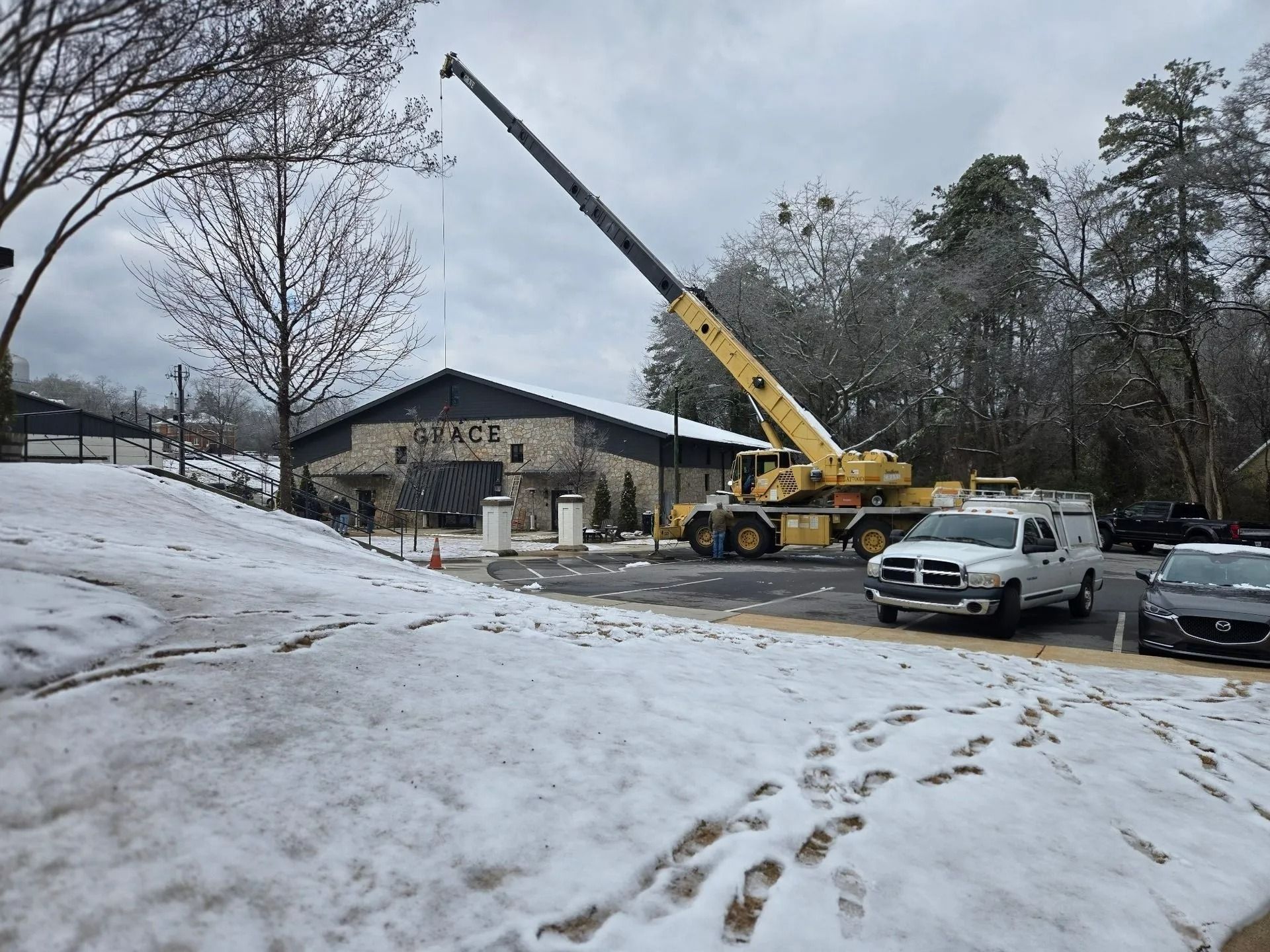 A yellow crane next to a building on a snowy day. A white truck and cars are also present.