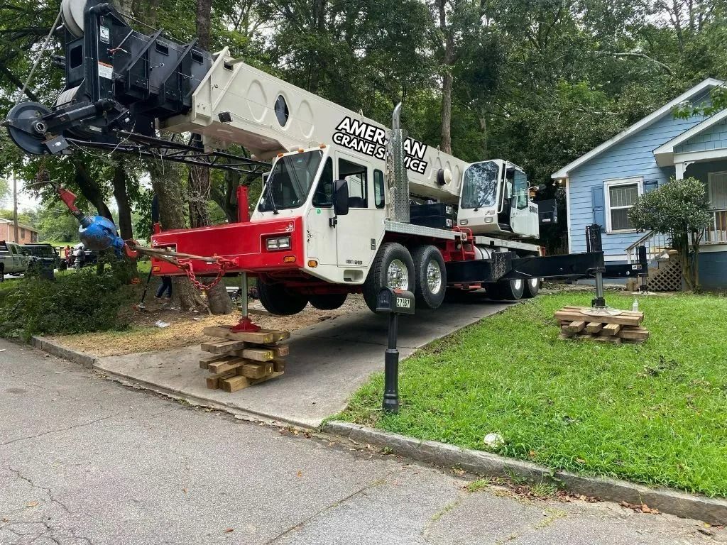 A white crane lifting something near a blue house on a residential street.
