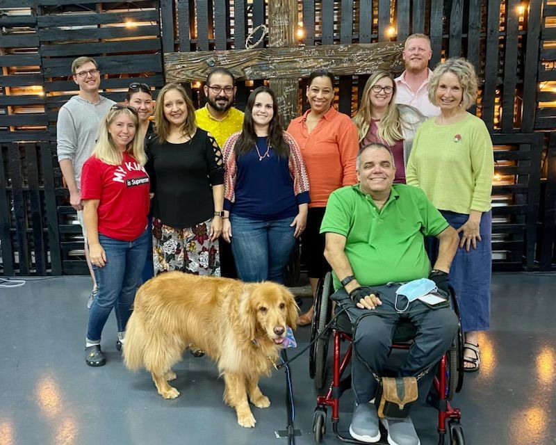 A group of people posing for a picture with a dog and a man in a wheelchair.