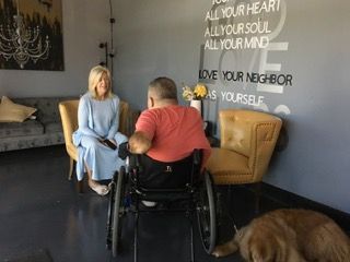 A man in a wheelchair is talking to a woman in a living room.