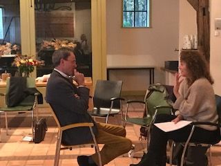 A man and a woman are sitting in chairs talking to each other.