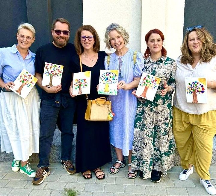 A group of people standing next to each other holding paintings of trees