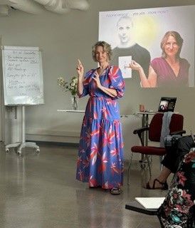 A woman in a blue dress is giving a presentation in front of a projector screen.