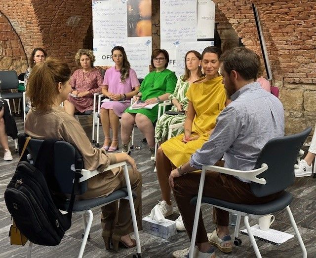 A group of people are sitting in a circle in front of a brick wall.