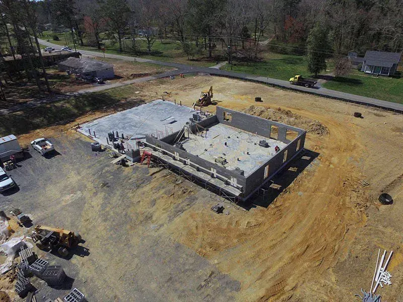 Construction site with foundation and partially built concrete building; heavy machinery and trucks are present.