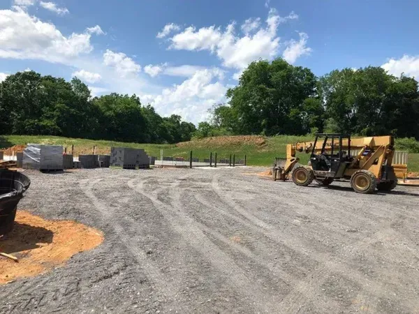 Construction site with a yellow forklift, gravel ground, and piles of materials under a cloudy sky.