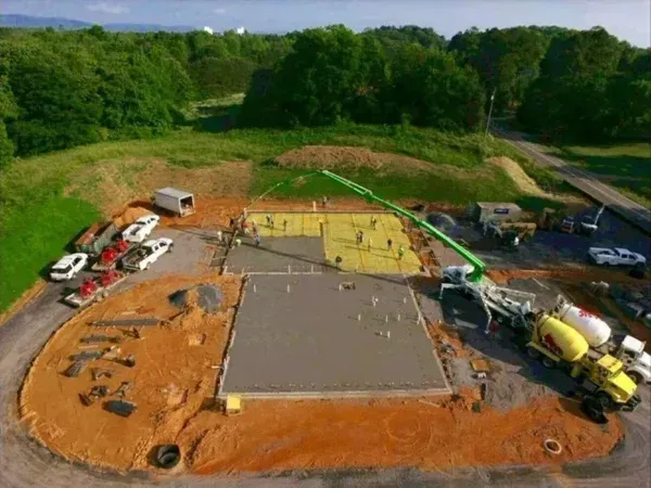 Construction site, aerial view: concrete being poured for a building foundation, with surrounding vehicles and equipment.