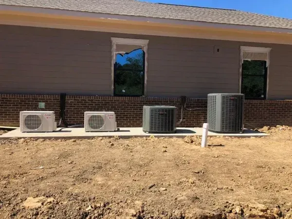 Exterior of a building with AC units. A row of four units sits on concrete next to the building's brick foundation.