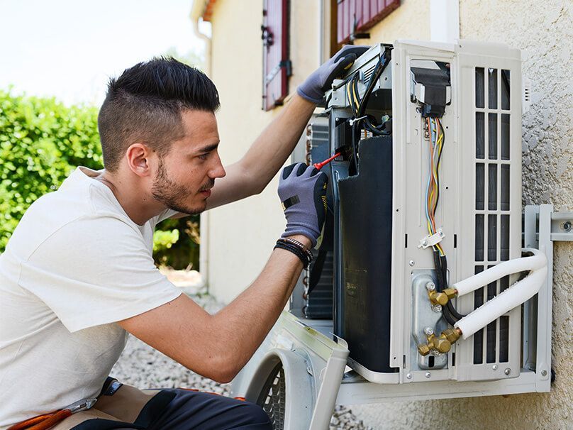 HVAC technician servicing an outdoor air conditioning unit. Gray gloves, testing electrical components.
