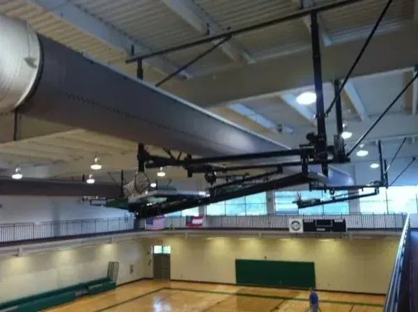 Basketball court with retractable hoops, viewed from an upper level. Green wall and bleachers visible.