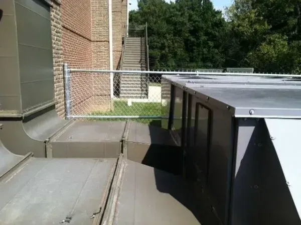 Rooftop view of HVAC equipment and a chain-link fence near a brick building with stairs.