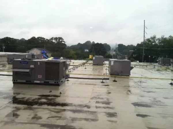 Rooftop with several gray HVAC units, overcast sky, trees in background.