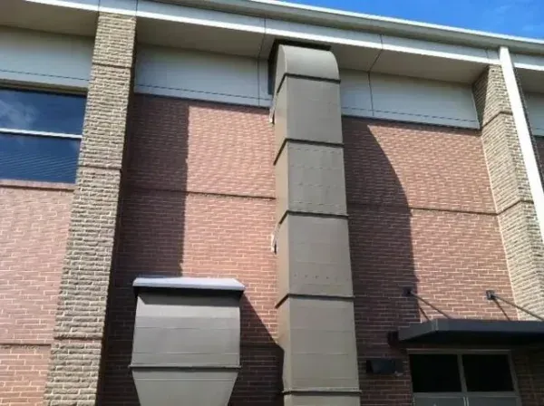 Exterior of a brick building with a large rectangular vent and box-like structure on the wall.