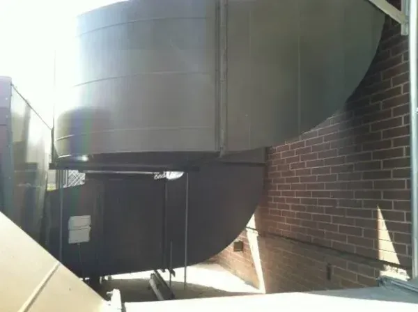 HVAC ductwork, metallic gray, against a brick wall. Sunlit, exterior setting.