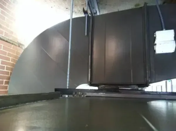 Large gray ventilation ductwork with a curved section, attached to a metal base, in an industrial setting.