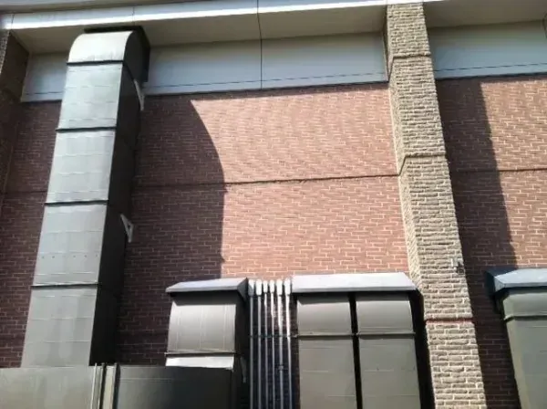 Exterior building with brick wall, metal air ducts, and decorative stone column.