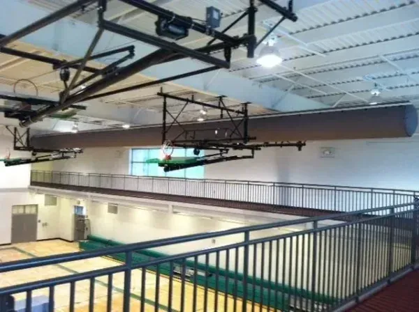 Indoor gymnasium with a balcony, basketball hoops, and dark support structures.
