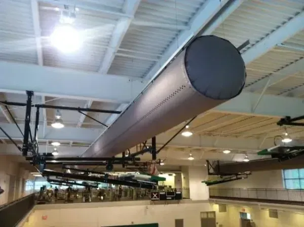 Gray cylindrical HVAC duct suspended from the ceiling in a gymnasium with basketball hoops.