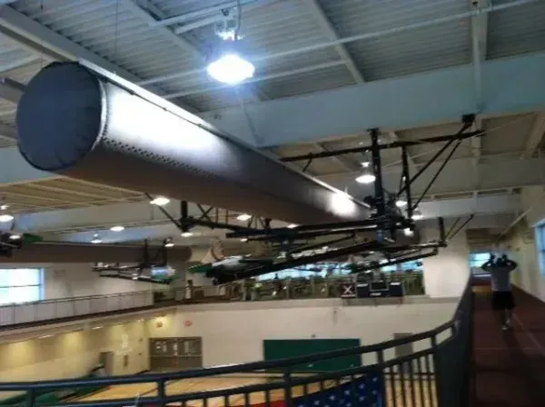 Indoor track and field facility with a runner on the track and suspended cylindrical structures.