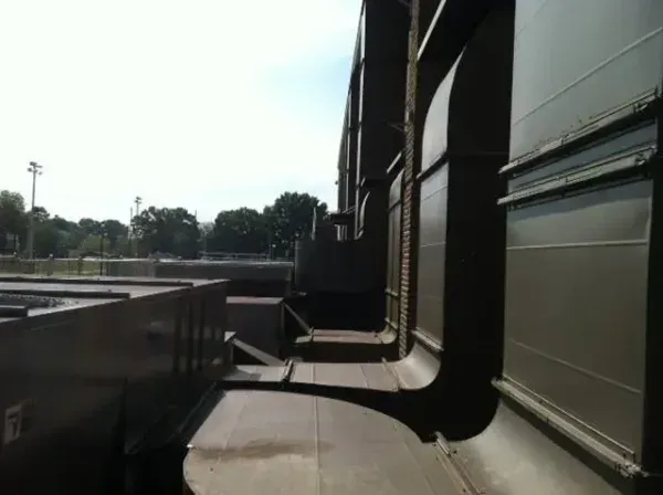 Side view of a large, olive-colored industrial structure with metal panels and sky in the background.