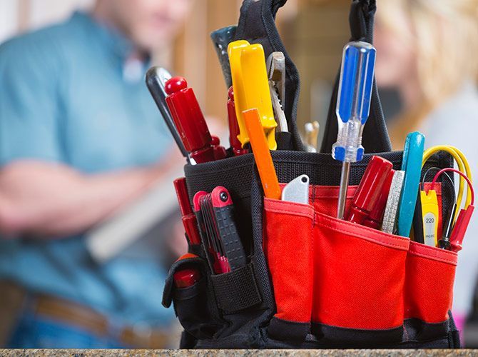 Red and black tool belt filled with various tools, with blurred figures in the background.