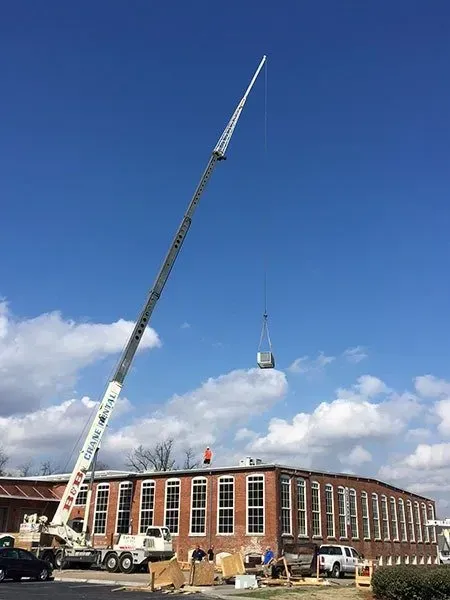 A crane lifts a small box toward a red-brick building under a blue sky.