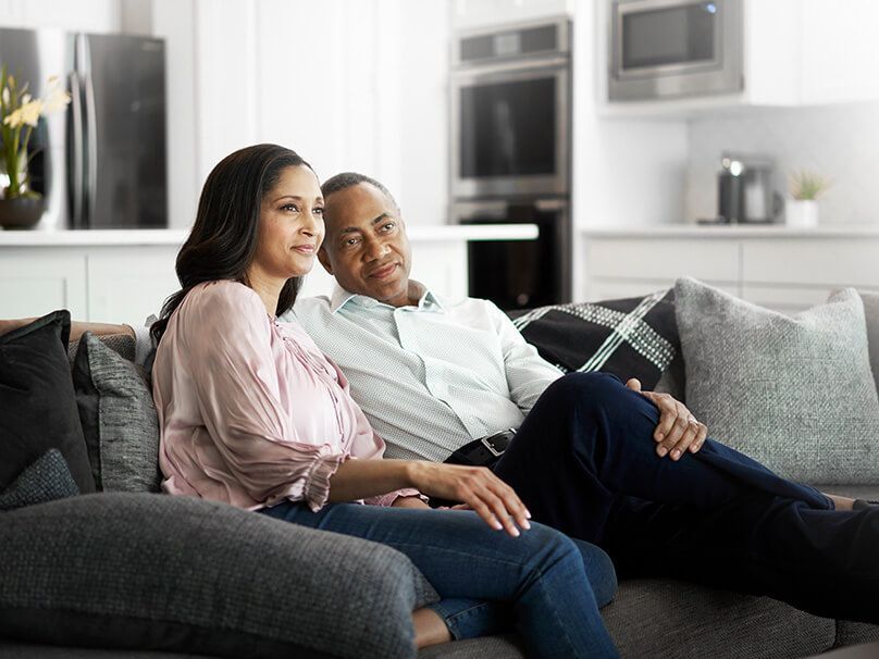 Couple sitting on a gray couch in a modern living room, looking off-camera.