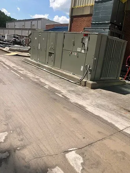 Large industrial HVAC unit on a concrete pad outdoors, with utility cables and a building in the background.