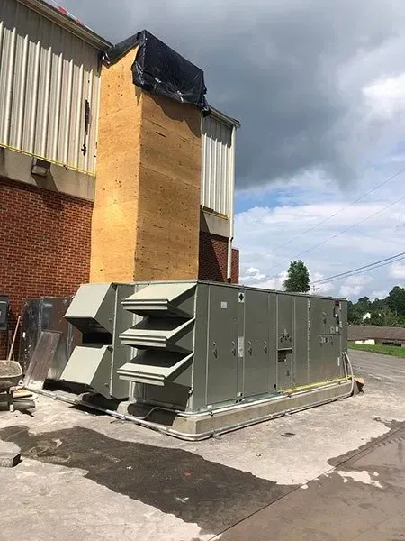 Large HVAC unit on a concrete pad next to a brick building with a damaged roof.