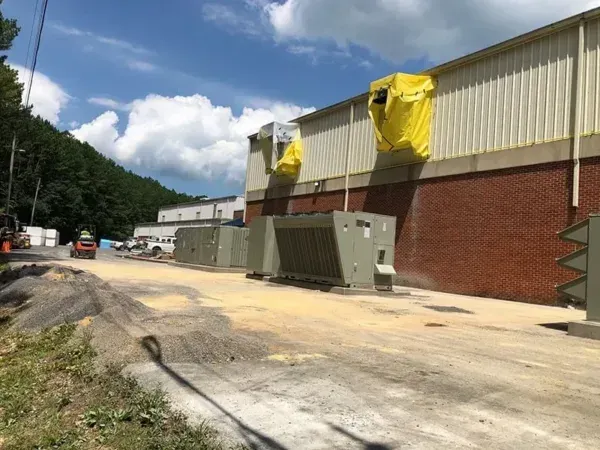 Industrial building exterior with electrical equipment, yellow covering, and gravel road.