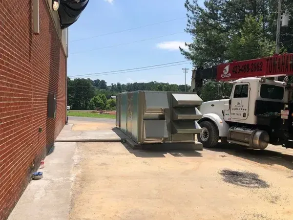 A large HVAC unit being lifted by a crane next to a brick building. Truck is visible.