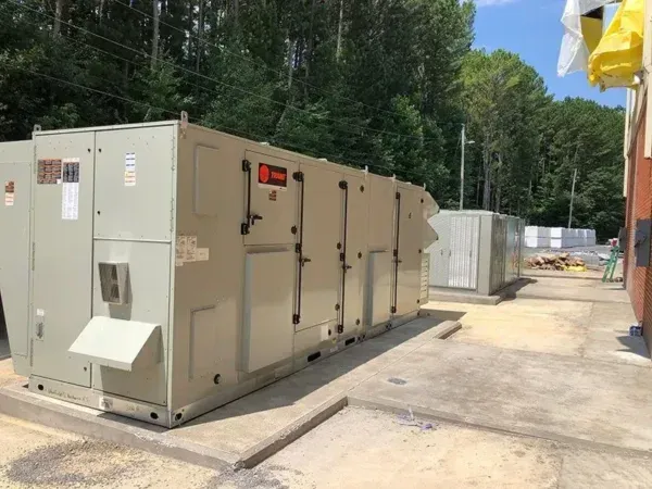 Large industrial HVAC units on a concrete pad near a building, with trees in the background.