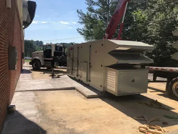 HVAC unit being unloaded by a crane next to a brick building.