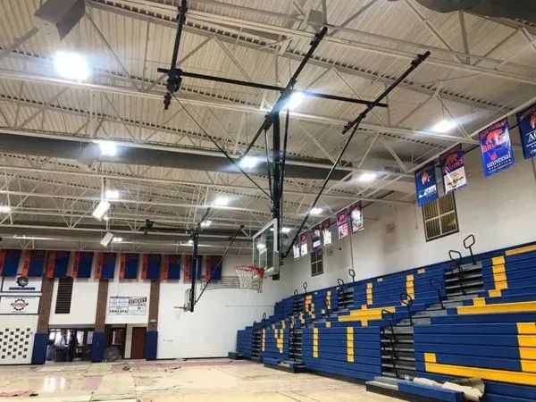 Basketball court interior with blue and yellow bleachers, banners, and overhead hoops.