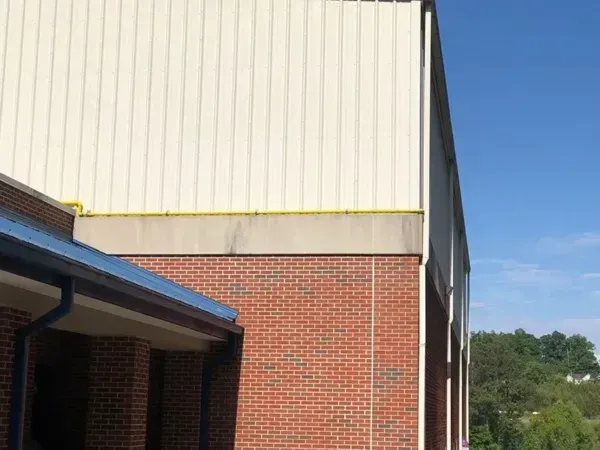 Exterior of building with brick, white siding, and blue roof against a blue sky.