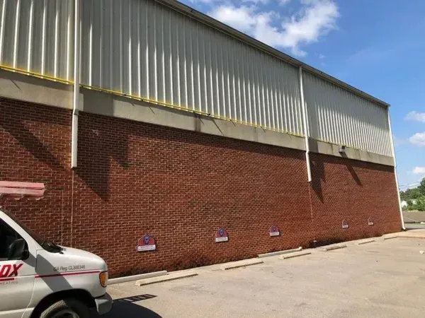 Brick building exterior with metal roof, parked van, and blue sky.